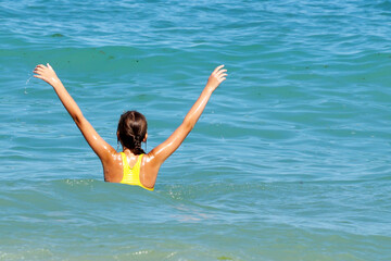 girl with hands up in the sea, rear view