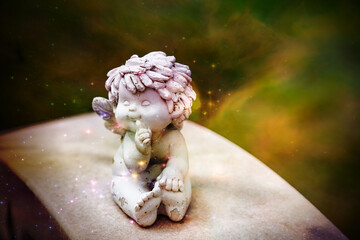 Ein kleines Kind sitzt als Engel im Sternenstaub auf einem Stein und lutscht am Daumen 