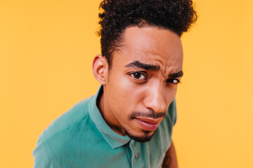 Obraz premium Close-up portrait of curious african guy with black hair. Indoor shot of brunette male model isolated on yellow background.