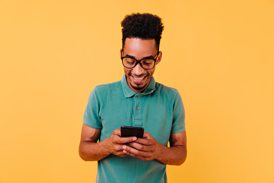 Handsome Black Guy In Big Glasses Reading Phone Message. Studio Portrait Of Pleased African Man Holding Smartphone.