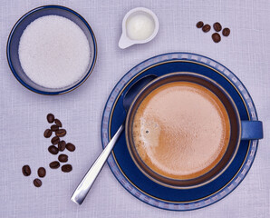 Coffee from above with blue crockery and a scattering of coffee beans with milk and cream.