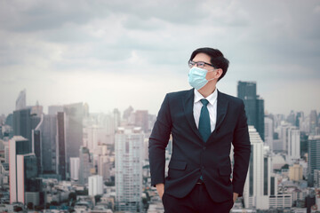 Fototapeta na wymiar Young Asian businessman in suit wearing face mask to protect himself against virus with skyscraper city outdoor, or anti air dust pollution problem in city