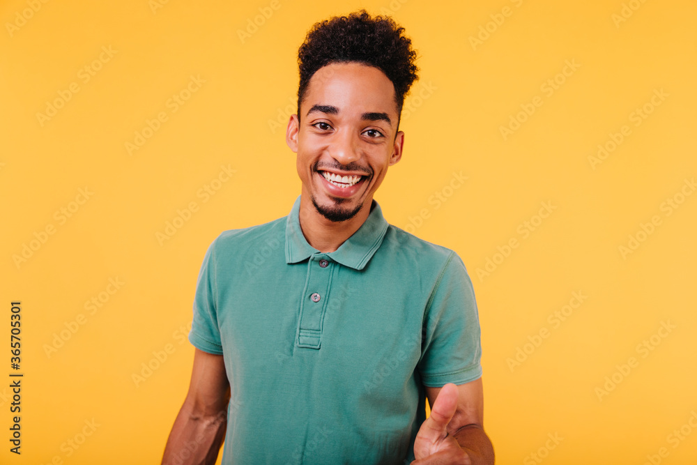 Wall mural Dark-eyed cheerful african guy expressing good emotions. Indoor photo of well-dressed male model in green t-shirt.