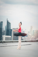 Fototapeta premium Asian ballerina dancer girl practicing ballet dancing on rooftop with skyscraper city view, adorable child dancing in ballet
