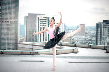 Fototapeta na wymiar Asian ballerina dancer girl practicing ballet dancing on rooftop with skyscraper city view, adorable child dancing in ballet