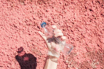 We are against plastic garbage. A hand in protective gloves clutches an empty disposable bottle.