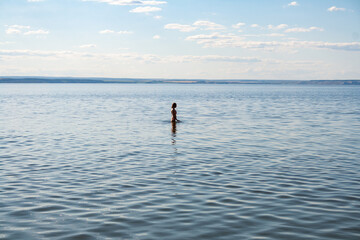 A young girl in the summer in the river, standing waist-deep in water.