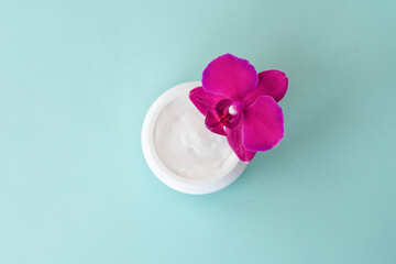 Fototapeta na wymiar Cream in white jar on mint background with beautiful bright magenta orchid flowers. Soft cream with orchid extract for moisturizing skin. Eco cosmetic product, top view