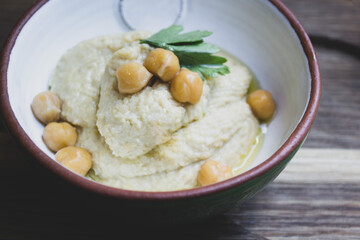 Hummus decorated with parsley and chickpea peas in a ceramic bowl on a wooden background 
