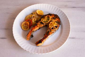 A slice of Salmon with parsley pieces and slices lemon and potato that is baked in the oven