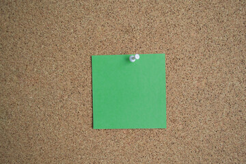 A green paper note on a cork Board, attached with a white pushpin. Copy space