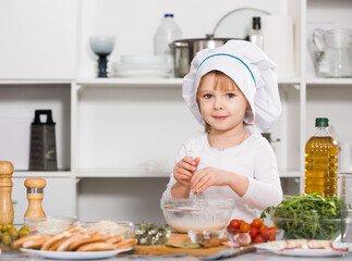 Smiling girl is cooking sauce for dish alone in the kitchen at home.