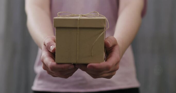 Slow motion young woman stand and show brown gift box with twine bow