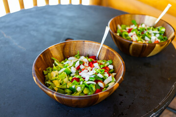 Closeup of fresh two large salad wooden bowls plates with lettuce and bell peppers on terrace of rustic log cabin building and nobody