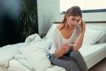 Obraz premium Upset woman sitting sad in white bed with negative pregnancy test