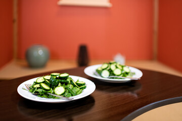 Wooden table and green salad meal with Japanese cucumbers and mizuna greens at home house interior in ryokan hotel or domestic room with traditional alcove in blurry background