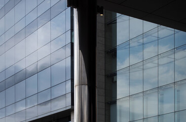 Obraz premium modern glass office buildings behind a steel column with blue sky clouds and sunlight reflected in glass windows