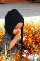 Autumn portrait of 2-3 years old child in garden. Fall season. Close-up view of cheerful sweet mixed-race baby boy in knitted cap