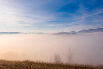 Beautiful sunrise over autumn mountain hills. Panoramic landscape with fog in the valley between mountain hills with trees on the slope.