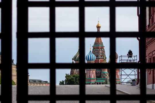 Saint Basil's Cathedral is visible through blurred lattice of closed metal gates. Clouds on the sky. Theme of censorship and restrictions in Russia.