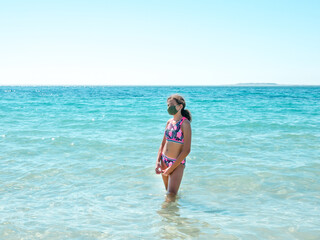 Teenage girl on the beach wearing a protective mask to prevent COVID - 19 or coronavirus disease, safe holidays concept