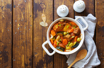 Beef meat and vegetables stew in white bowl on dark wooden table