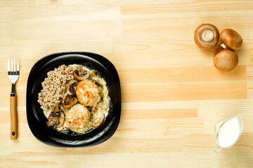 Chicken meatballs with mushrooms in a creamy sauce with a side dish of green buckwheat next to mushrooms and cream.