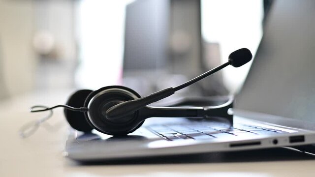 A female call center operator removes the headset and puts it on the laptop keyboard at the end of workday. Woman's hand working in customer support takes off the headphones.