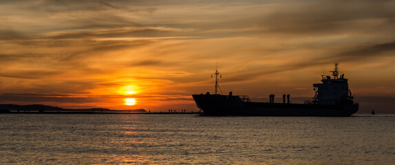 Fototapeta premium SUNSET BY THE SEA - An evening landscape by the sea coast and a ship going to the port 