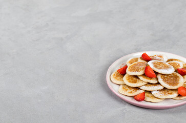 Mini pancakes with strawberries and powdered sugar on a plate on a light gray background copy space
