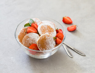 Mini pancakes with strawberries and powdered sugar in a glass bowl on a light background