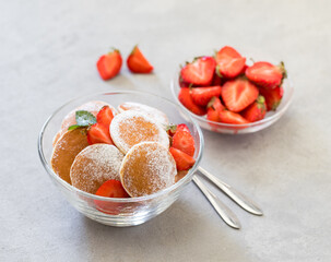 Mini pancakes with strawberries and powdered sugar in a glass bowl on a light background