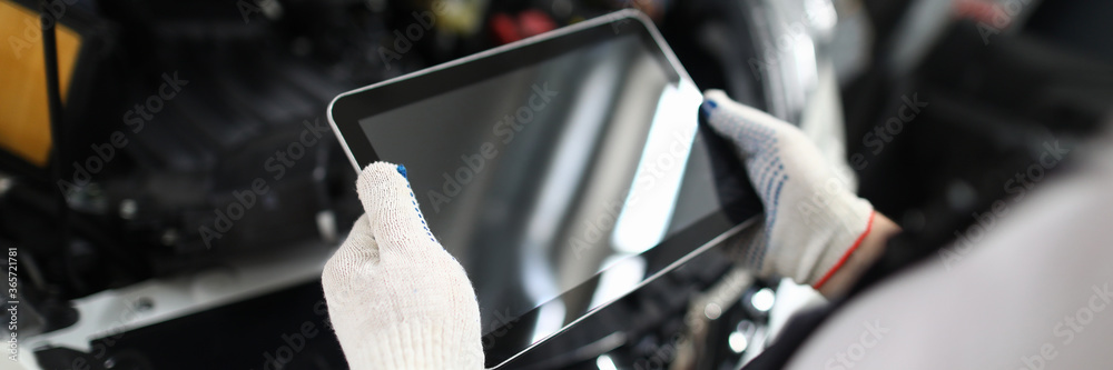 Wall mural close-up view of male mechanic holding digital tablet with black screen and copy space. open trunk. 