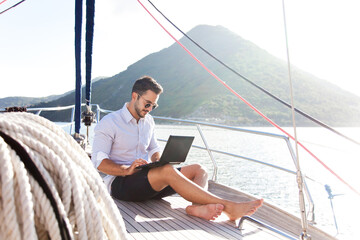 Man working on yacht office with laptop. Traveling on sailboat. Traveler using tablet computer....