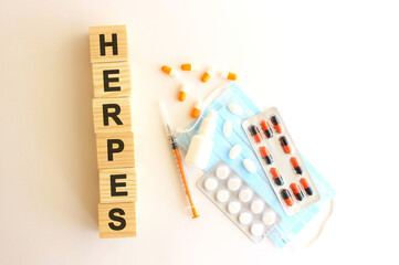 The words HERPES is made of wooden cubes on a white background with medical drugs and medical mask. Medical concept.