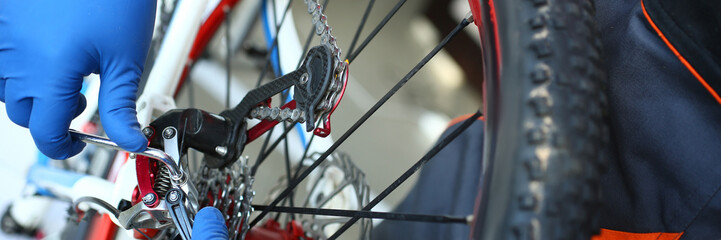 Close-up view of mechanic hands repairing mountain bike in workshop. Macro shot of bicycle wheel....