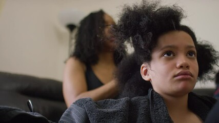 Young mixed race girl having her hair oiled and styled by a family member