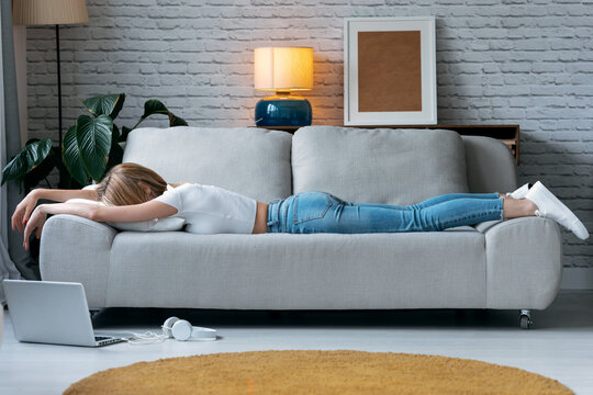 Exhausted young woman lying down on sofa at home.