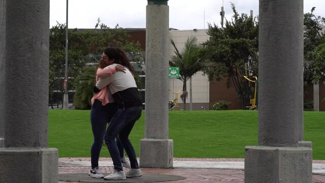 Joven pareja de amigos caucasicos corren para abrazarse, con fondo de parque mientras el hombre alza a la joven de piel morena y grian, en su primer encuentro tras la cuarentena del Covid-19.