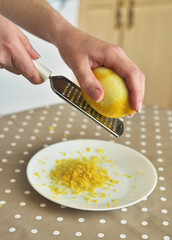 Closeup of woman rubbing lemon zest on grater