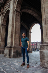 Fototapeta na wymiar Full body portrait of a young latin man standing right in front of a historic mexican building near downtown