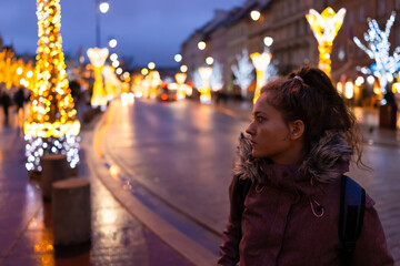 Warsaw, Poland old town at night with young tourist woman looking at illumination Christmas...