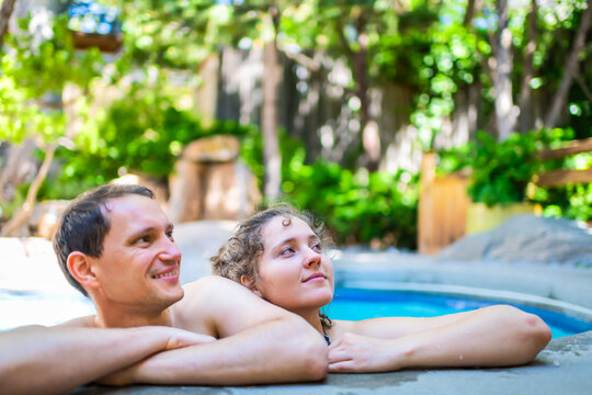 Young woman man happy romantic couple relaxing swimming leaning on stone railing edge of Japanese spa pool with colorful blue water in Japan onsen poolside