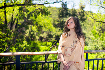 Naklejka premium Young caucasian woman dressed up in kimono costume by railing fence in outdoor garden zen home house