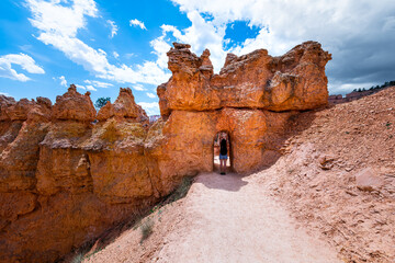 Young woman standing in desert landscape tunnel arch in Bryce Canyon National Park on Navajo loop Queen's Garden trail with sandstone rock formation