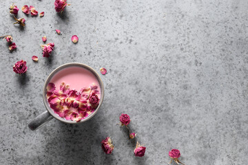 Rose moon milk in grey cup and rose petals on grey background. Top view. Copy space