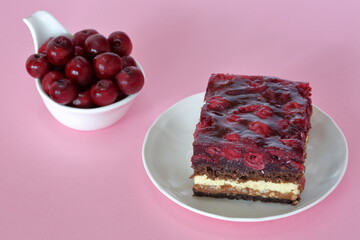 Cake with cherries and fresh cherries in white bowl  close up on pink background