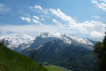Fototapeta premium Landscape above village Engelberg in canton Obwalden in Switzerland in the springtime. The mountaintops and peaks are still covered with snow but in lower altitutes is everything green.