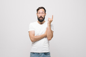 Naklejka premium Studio portret zaskoczonego, ładnego młodzieńca z krótką fryzurą stojącego na białym tle, zdziwionego patrząc na aparat ze skrzyżowanymi rękami na piersi