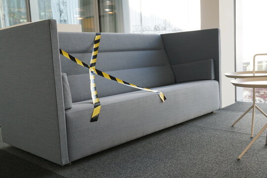 Social Distancing Rules Implemented In A Corporate Building To Stop Spreading Of Coronavirus And Covid-19. Sofas In Break Space Are Partly Blocked  With Barrier Tape To Keep Safe Distance.